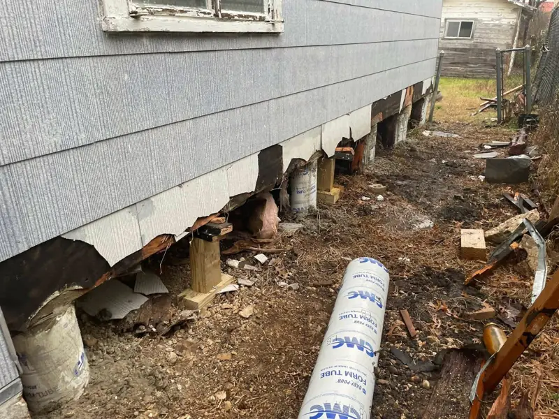 Crawl space opened along a house wall with new pier supports and a cardboard concrete form tube